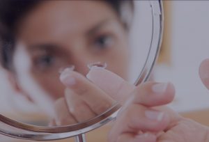 Woman starting her day by inserting her contact lenses after cleaning them by looking into a magnifying mirror